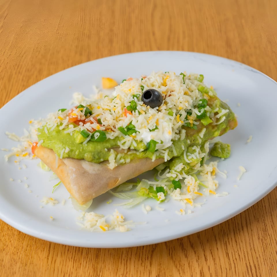 Crispy burrito topped with guacamole, rice, cheese, sour cream, green onions, and an olive.